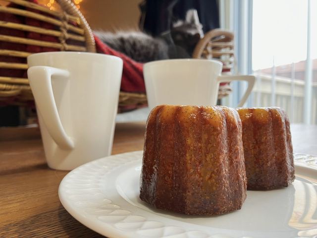 Two canelés on a plate beside coffee cups